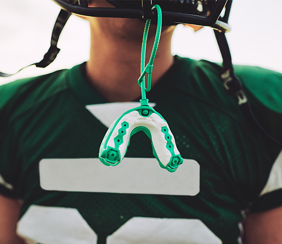 Teen with athletic mouthguard hanging from football helmet