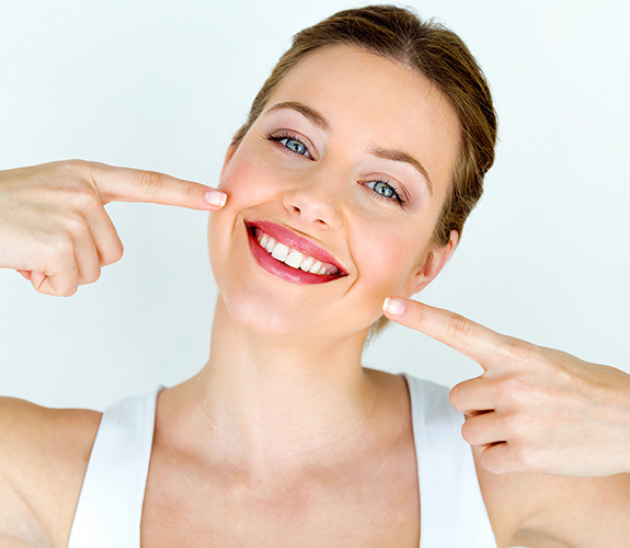Woman pointing to flawless smile after crown lengthening