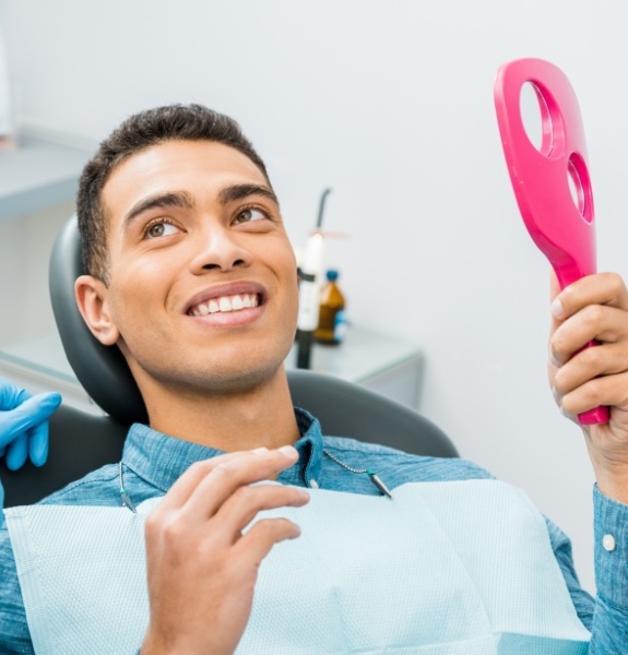 Man looking at his smile in mirror while talking to dentist