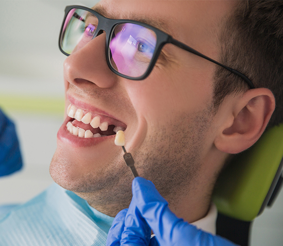 Man's smile compared with dental implant tooth replacement shades during consultation