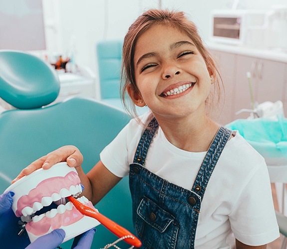 Father brushing daughter’s teeth while dentist looks on