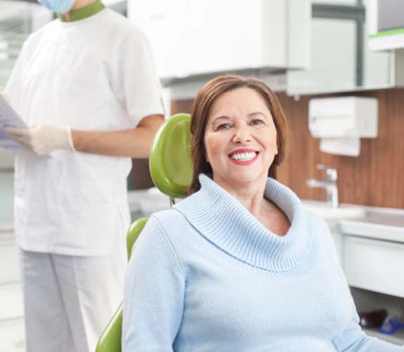 Woman sitting down in dental chair smiling after scaling and root planing in Channahon, IL