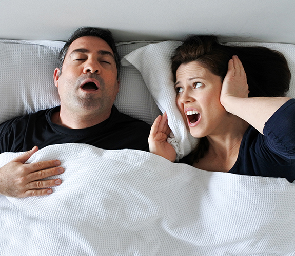 Frustrated woman next to snoring man who needs sleep apnea treatment