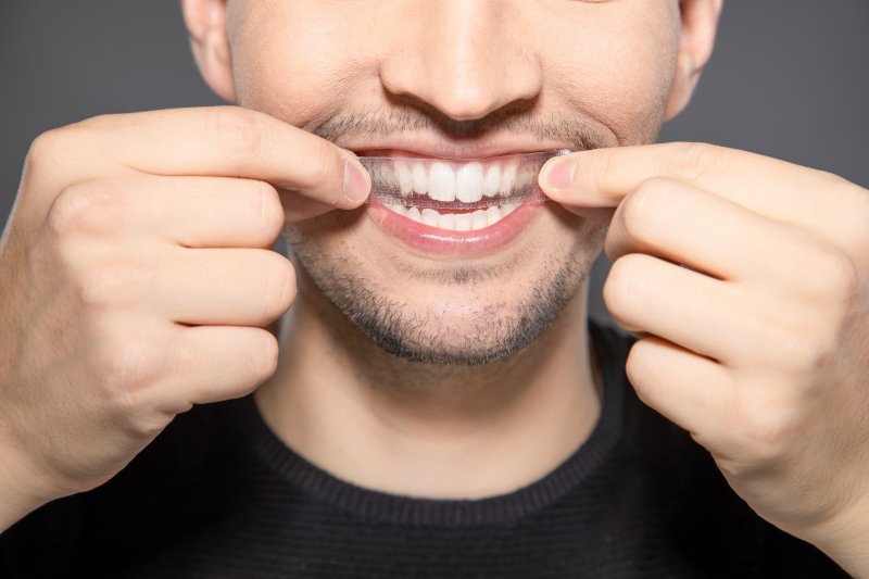man putting whitening strip on upper row of teeth